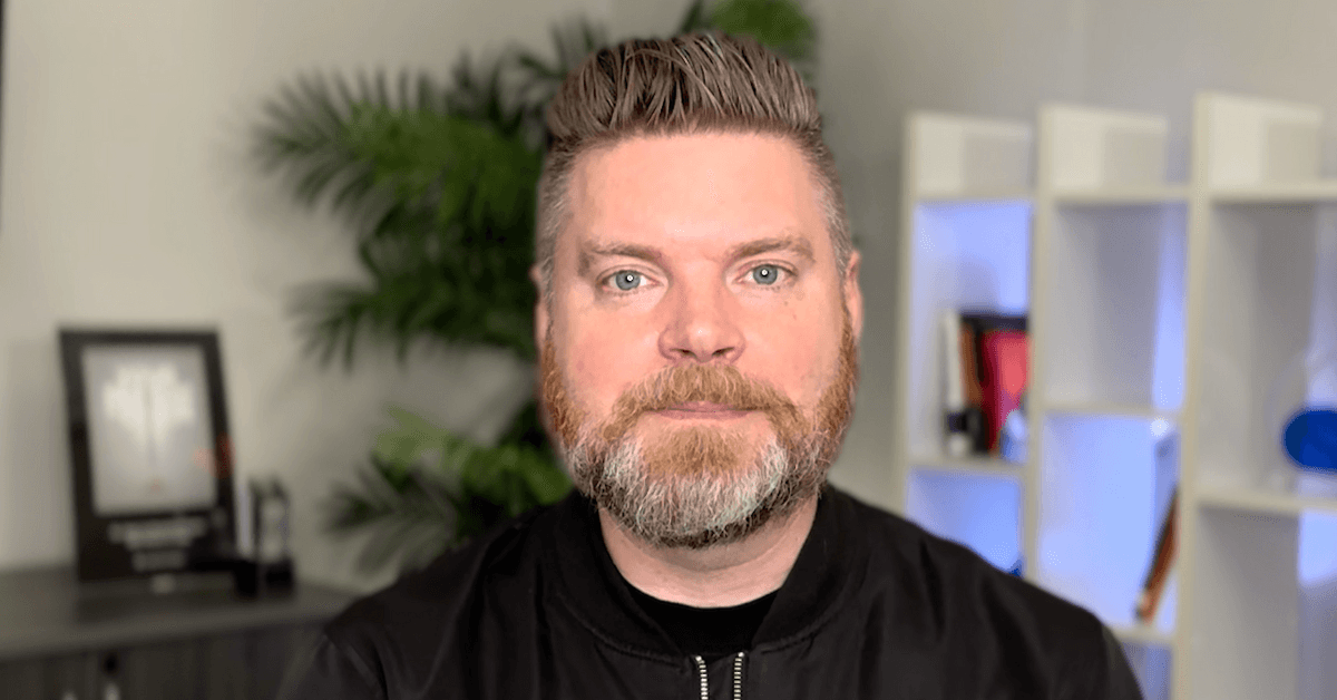 Andrew Aebersold, CEO of Mediaura, looks into the camera while explaining how the latest Google algorithm update has changed SEO for the healthcare industry. He is wearing a black zip up. The background is an office scene, featuring a bookshelf and plant.