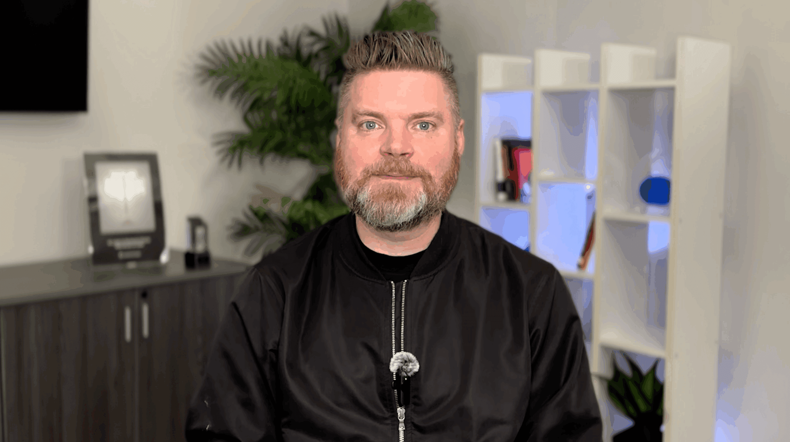 Andrew Aebersold, CEO of Mediaura, looks into the camera while explaining the importance of audience targeting and digital marketing and the most important groups to target. He is wearing a black zip up. The background is an office scene, featuring a bookshelf and plant.