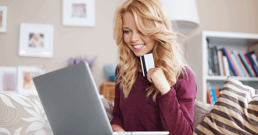 A smiling blonde woman in her living room contemplates an online purchase on her laptop, while holding her credit card. If you're advertising on Meta, the platform attempts to find your ideal customer during its learning phase.