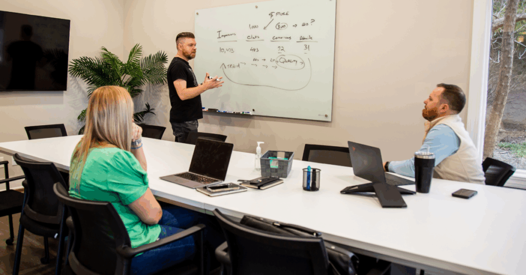 Team members for Mediaura, a full-service digital agency, discuss marketing concets while gathered around a conference table in a brightly lit room.