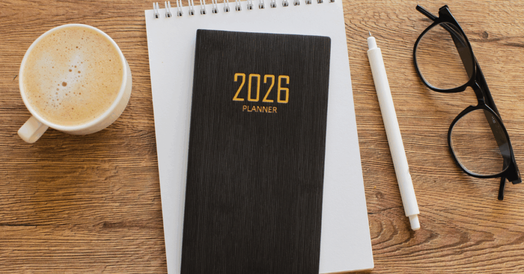 An image of a 2026 planner, coffee mug, white pen, and glasses — symbolizing the importance of planning your business strategy around 2026 digital marketing trends.