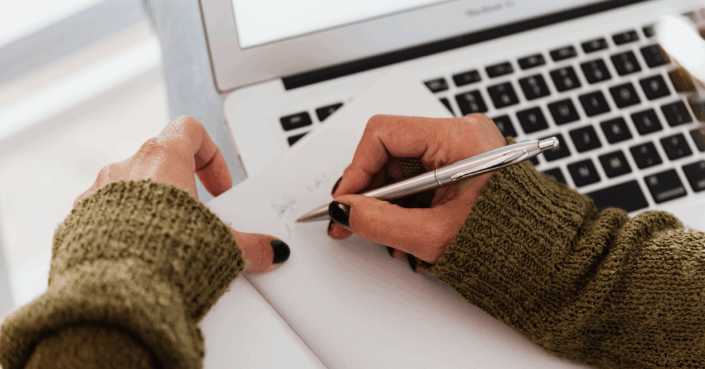 Woman strategizes on paper while she works on a laptop. Closeup of her hands writing in a notepad. A new competitor strategy is key when one emerges on the scene.