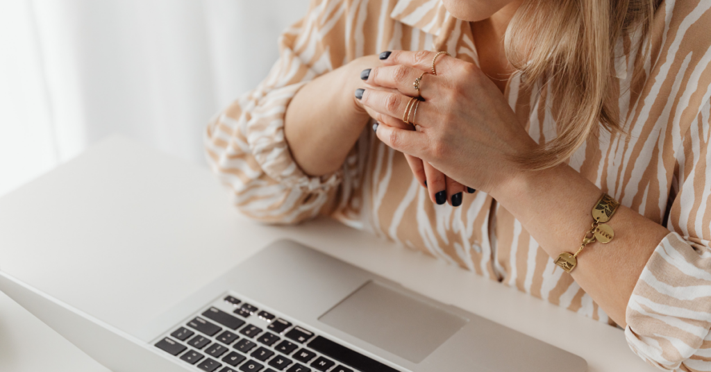 A woman in a put together outfit, sporting a striped blouse and lots of rings on her fingers leans over a Mac laptop, contemplating the impacts of the new Google Discover update.