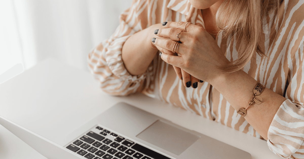 A woman in a put together outfit, sporting a striped blouse and lots of rings on her fingers leans over a Mac laptop, contemplating the impacts of the new Google Discover update.